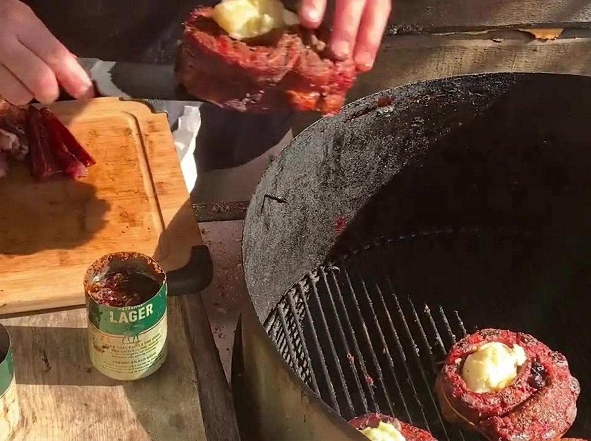 Placing a stuffed rib cup onto a charcoal grill next to another meat cup and thick slices of bacon.