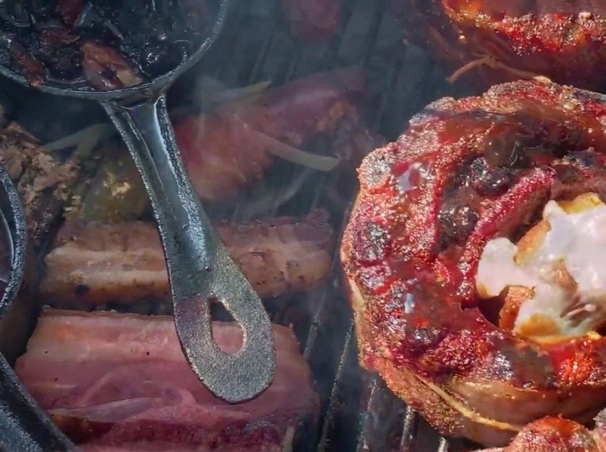 Shredded cheese melting over a dark, blueberry-glazed stuffed rib cup on a charcoal grill.