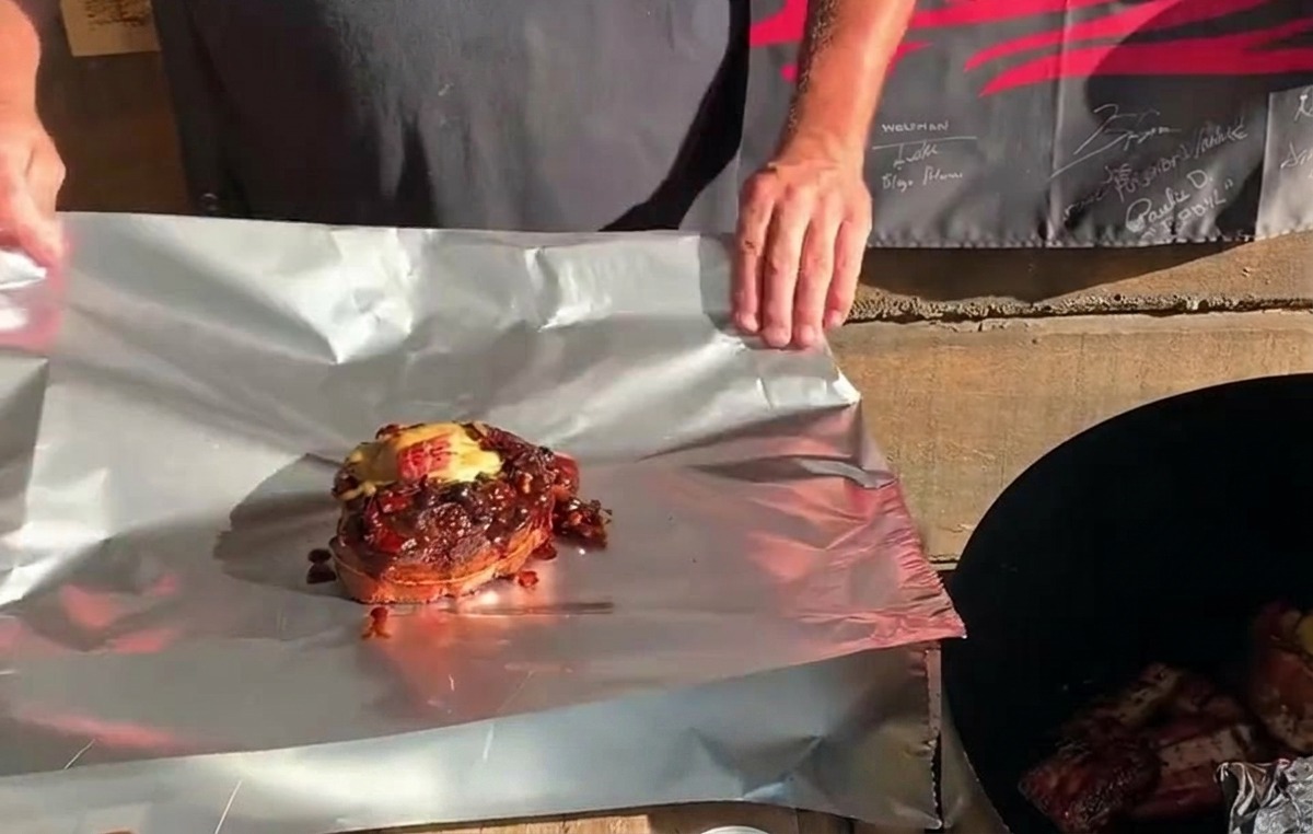 A fully stuffed St. Louis rib cup topped with cheese and sauce, sitting on a sheet of aluminum foil ready to be wrapped.