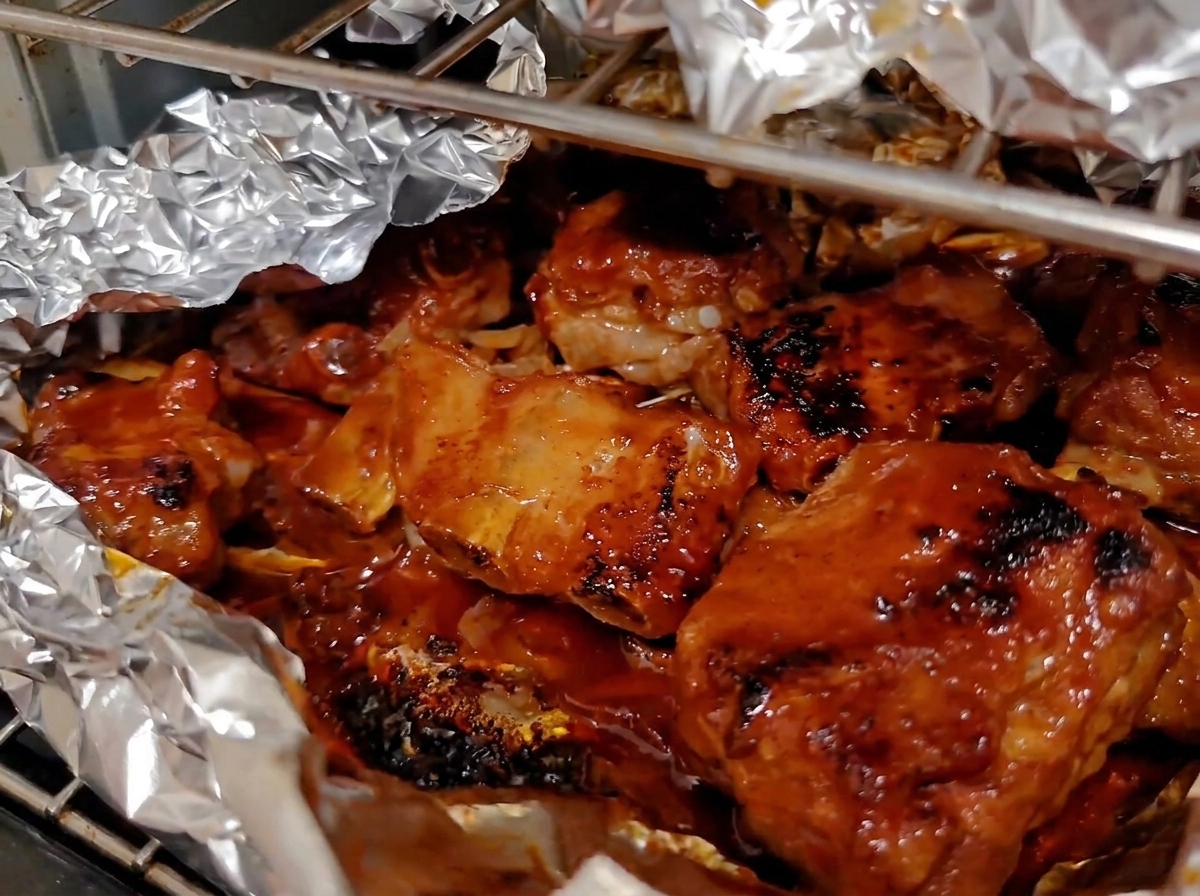 Deeply caramelized and glazed baked pork ribs bubbling inside an open aluminum foil lining in the oven.