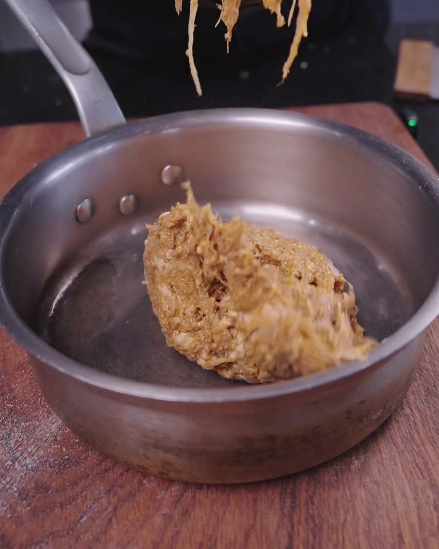 A mound of shredded savory pulled pork being heated inside a small metal saucepan.
