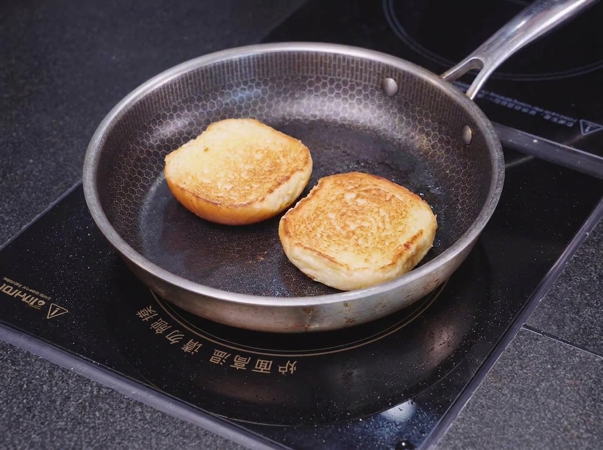 Two halves of a brioche bun toasting face-down in a honeycomb-patterned skillet until the edges are golden and crisp.