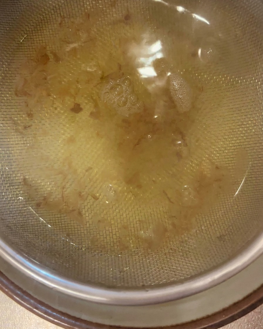 Clear golden dashi broth being filtered through a stainless steel mesh strainer into a bowl below.