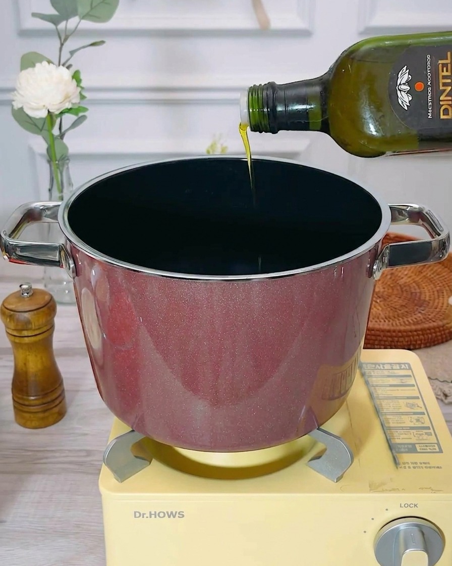 Extra virgin olive oil being poured into an empty, preheated cooking pot.