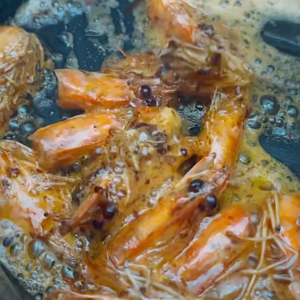 Shrimp heads being lifted from the seasoned oil using cooking chopsticks.