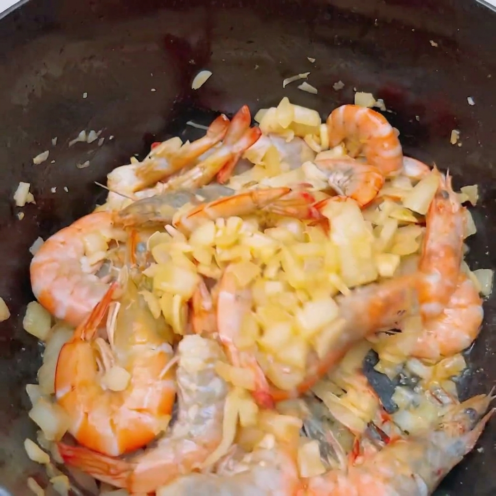 Freshly sliced tomatoes being added to a pan with pink, partially cooked whole shrimp.