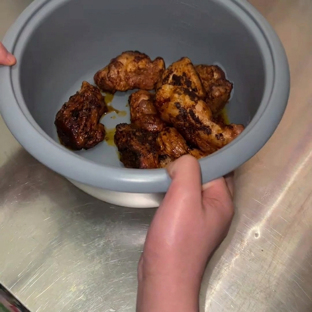 A person holding the grey inner bowl of a rice cooker filled with golden-brown fried pork chunks.