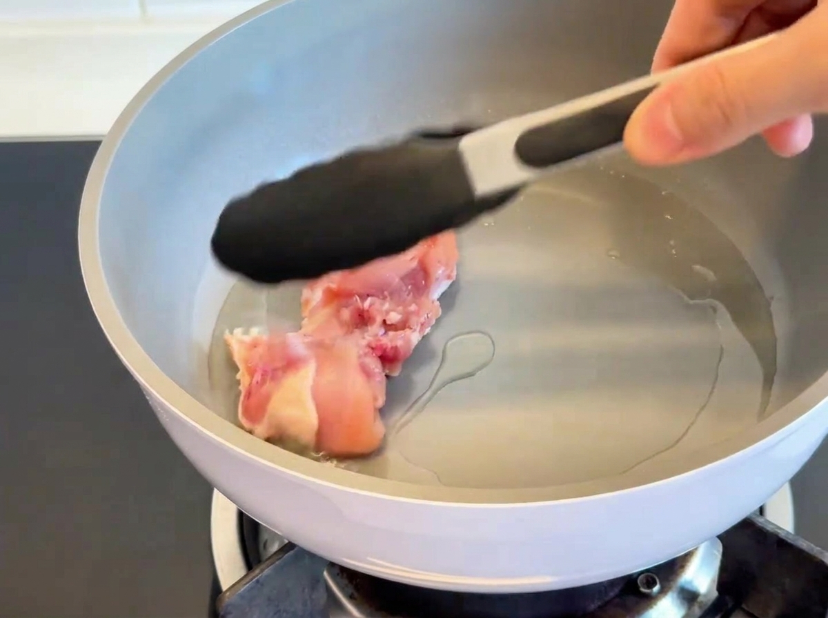 Chicken thighs being pan-seared skin-side down in a hot pan, showing golden-brown crispy skin.