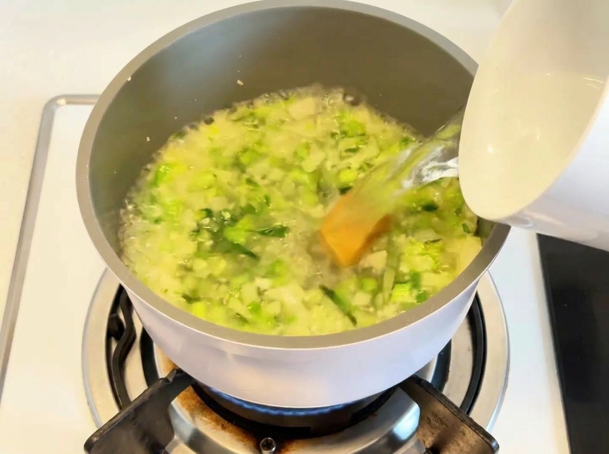 Water being poured into a pot containing sautéed vegetables and soup base.