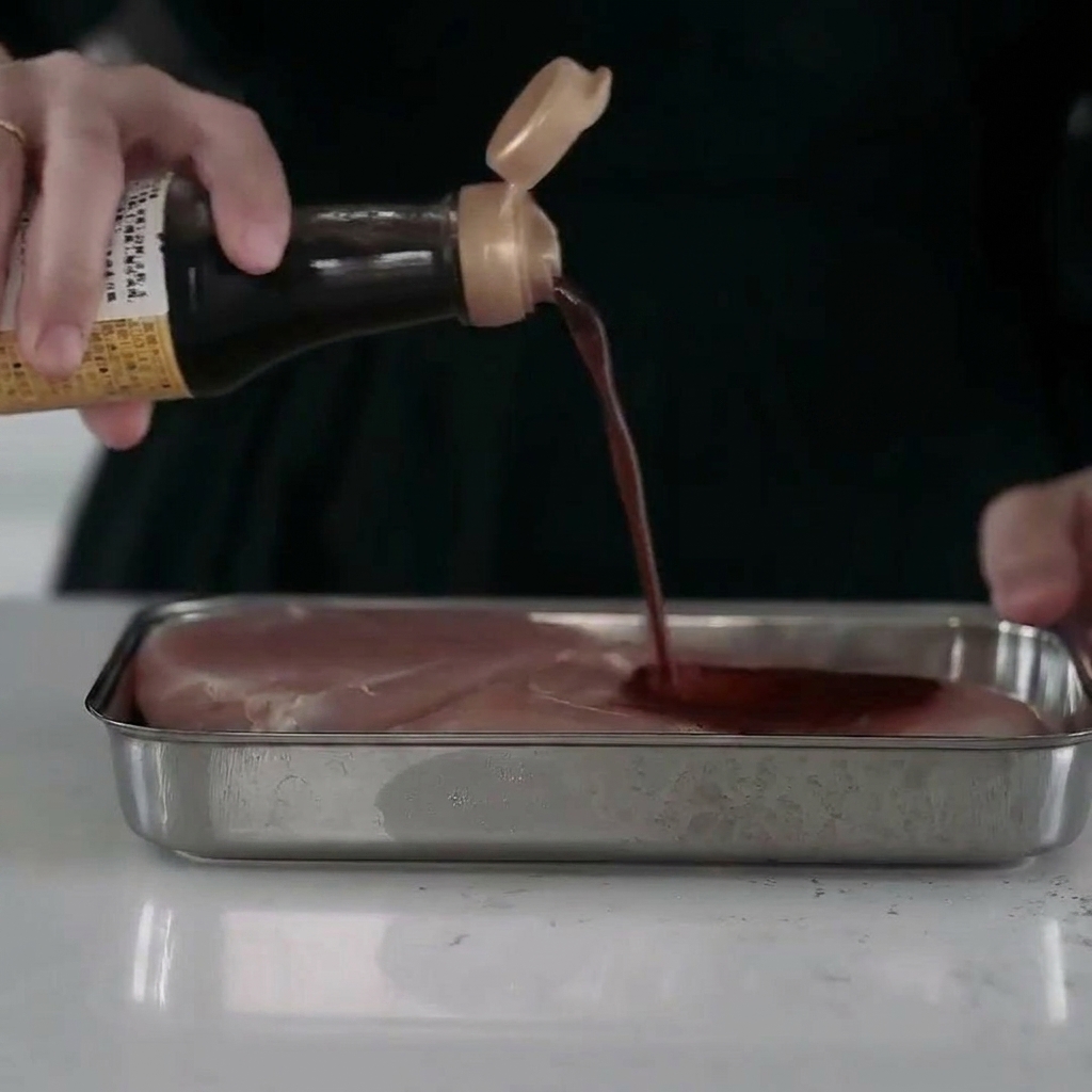 Juicy chicken breast pieces resting in a metal tray, fully coated in a flavorful liquid marinade.