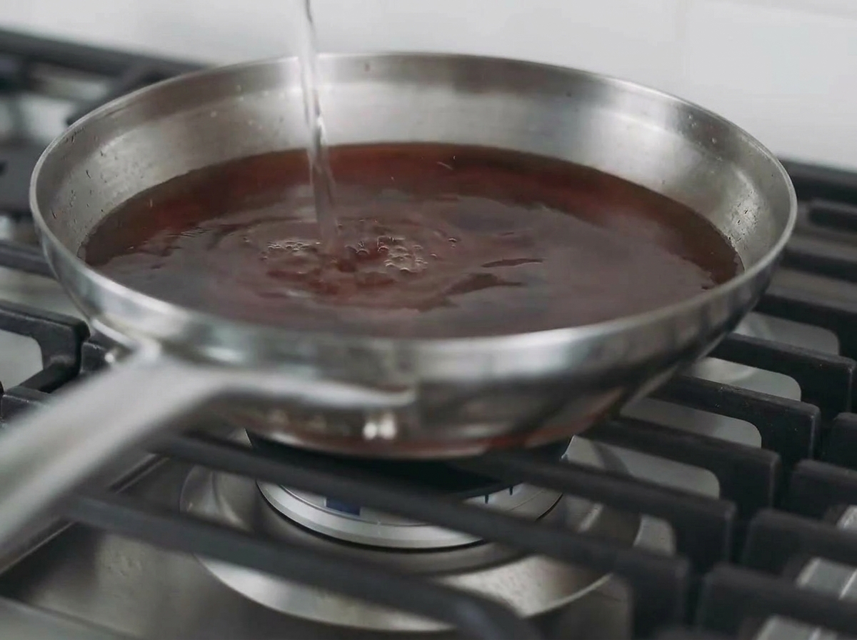 Liquid being poured into a pan containing a seared chicken breast to create a broth.
