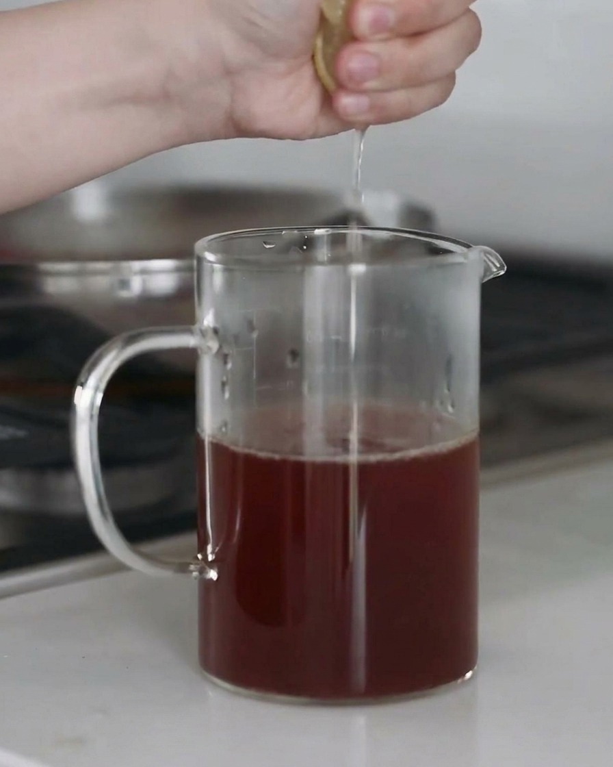 Fresh lemon juice being squeezed into a bowl of seasoned soup broth, with droplets captured mid-air.