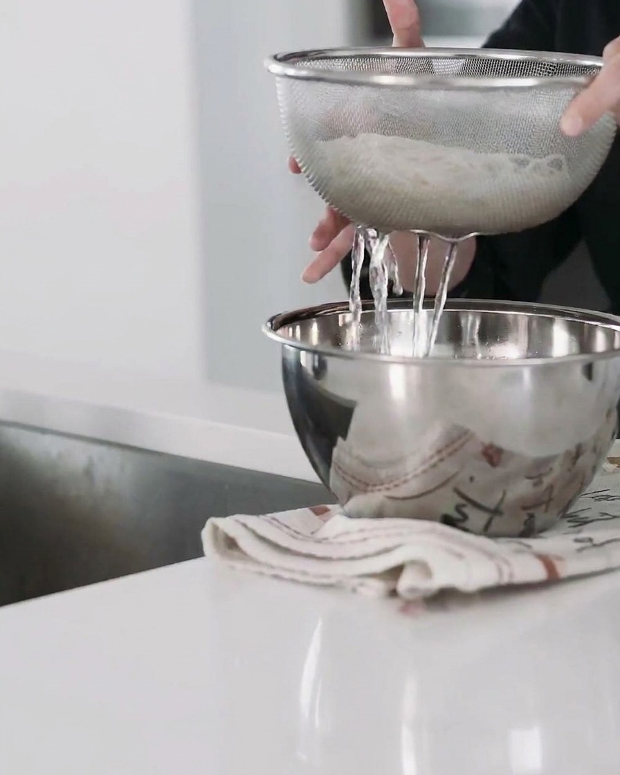 Cooked udon noodles being drained in a metal colander.