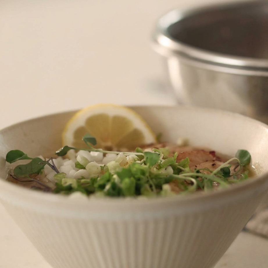 A bowl of chilled noodles in broth topped with diced onions, green onions, and black pepper.