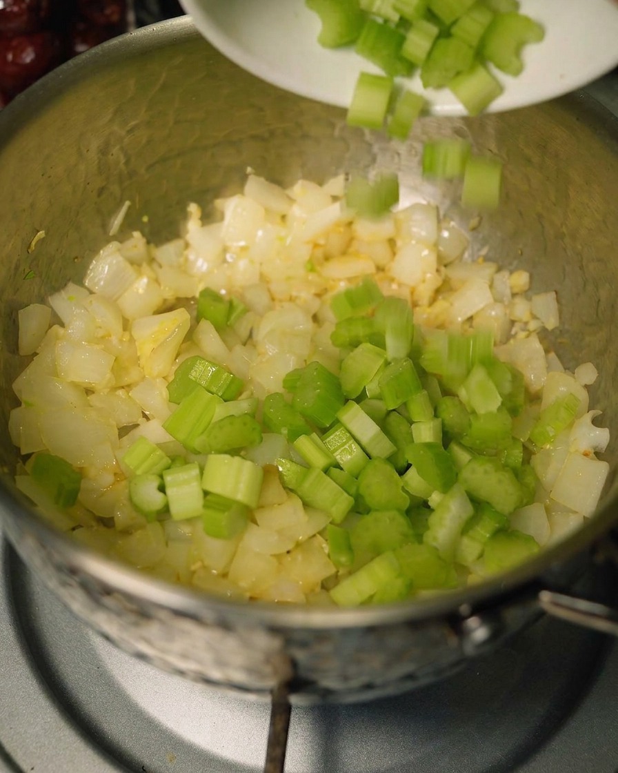 Celery and carrots being added to a pot of sautéed aromatics.