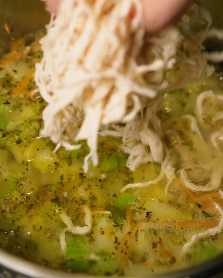 Shredded chicken being added to a pot of simmering soup.