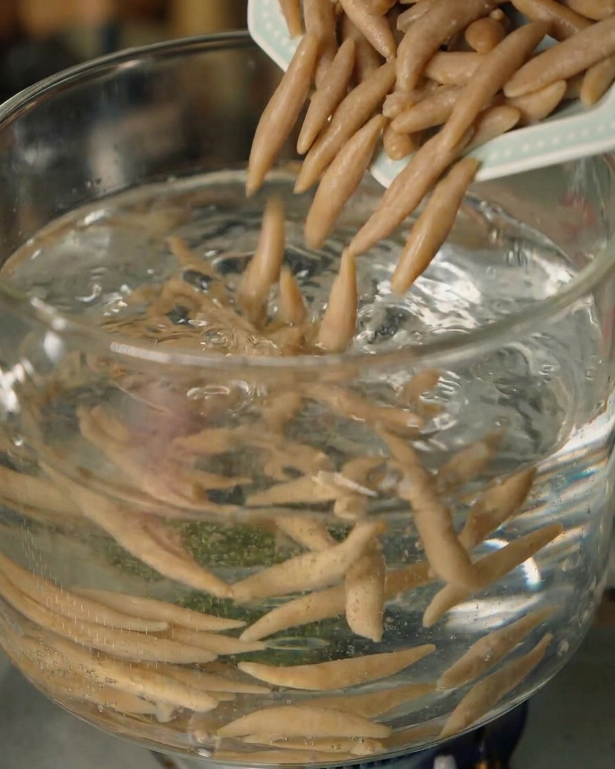 Shanxi oat fish noodles being dropped into a pot of boiling water.