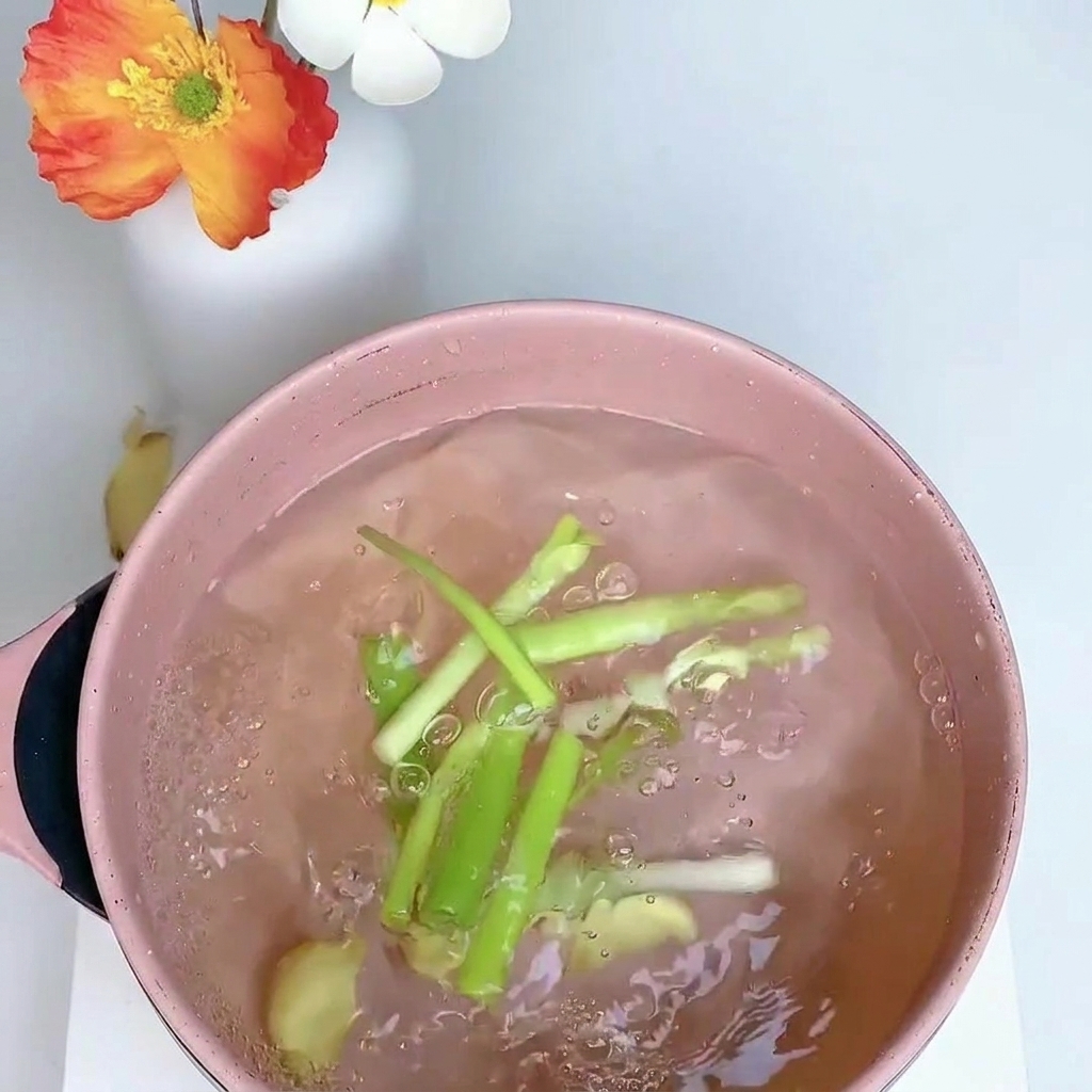 Chicken leg simmering in a pot of water with scallions, ginger, and star anise.