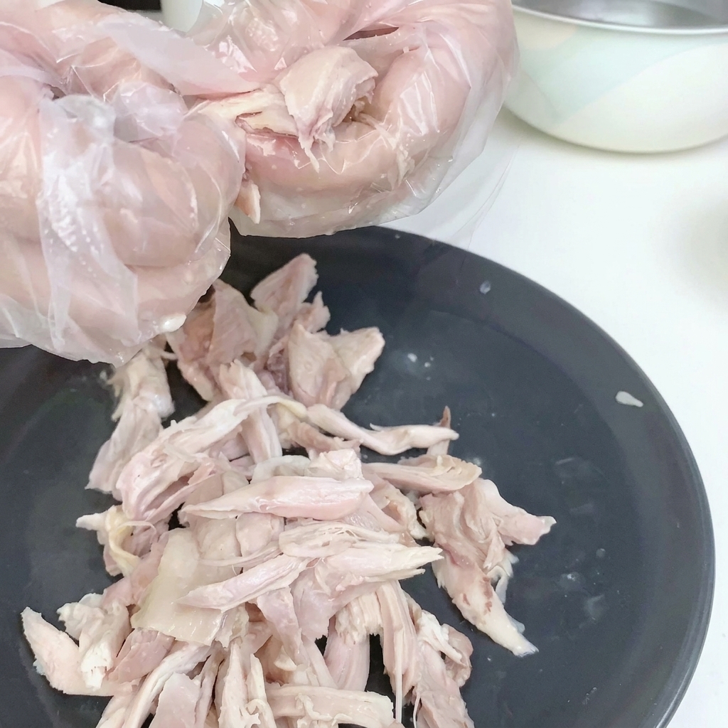 Shredded chicken meat on a white plate, skin removed.