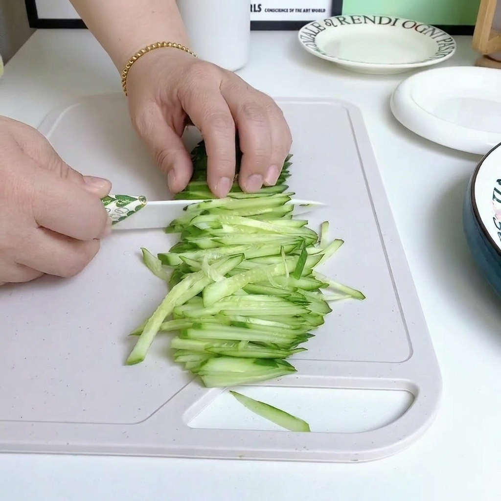 Fresh cucumber being sliced into thin strips on a wooden cutting board.