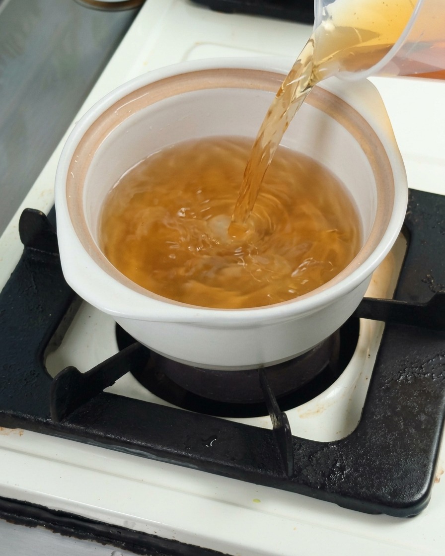 Kombu dashi broth being poured into a white ceramic pot, preparing the base for cooking.
