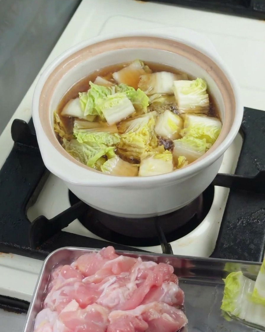 Chopped baby bok choy simmering in broth inside a white ceramic pot with the lid placed on top.
