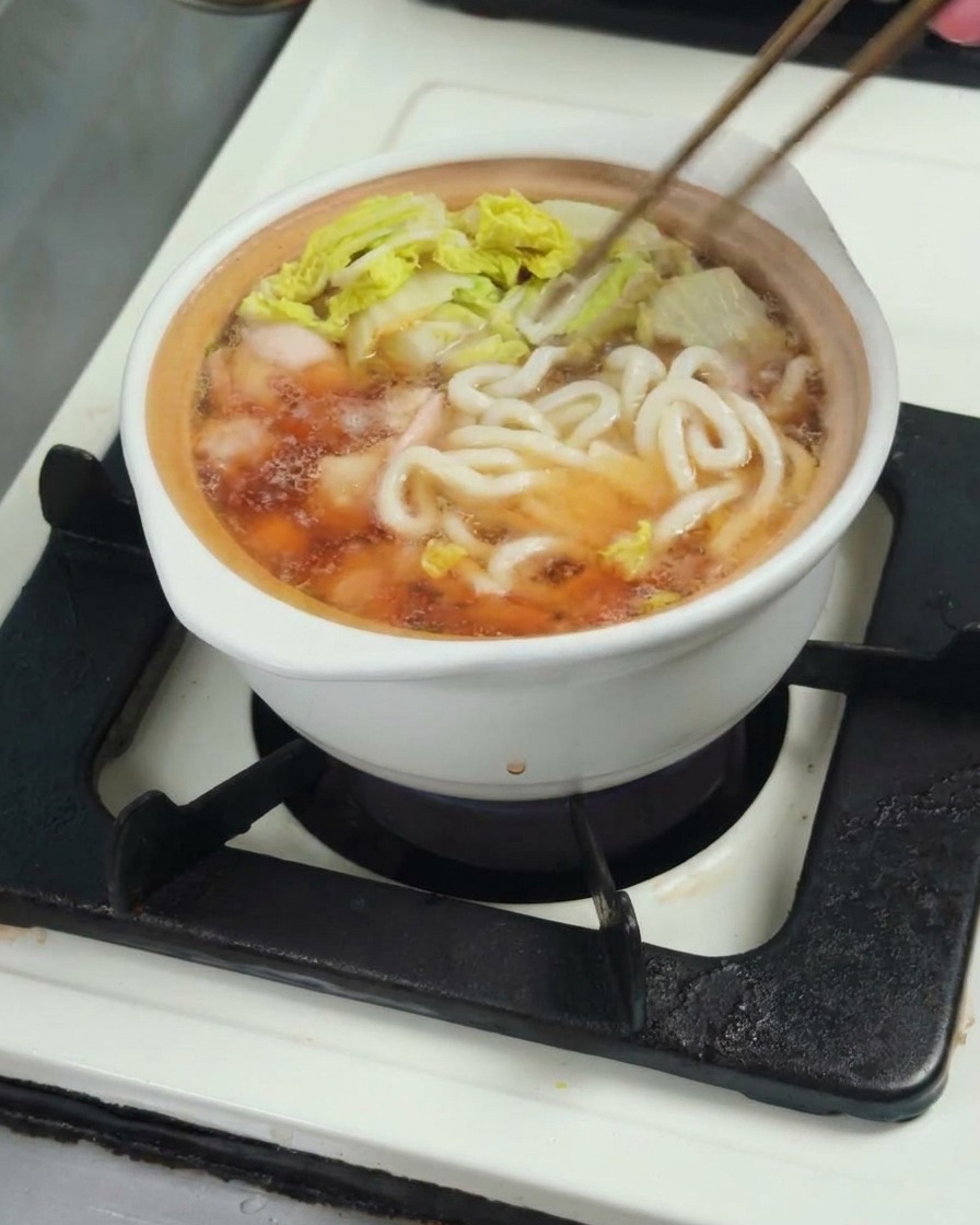 Udon noodles being added into the pot of broth, chicken, and bok choy to finish cooking.
