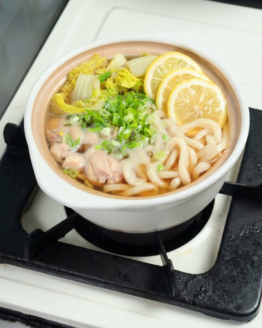 Fresh yellow lemon slices being carefully placed over the top of a steaming bowl of udon noodles.