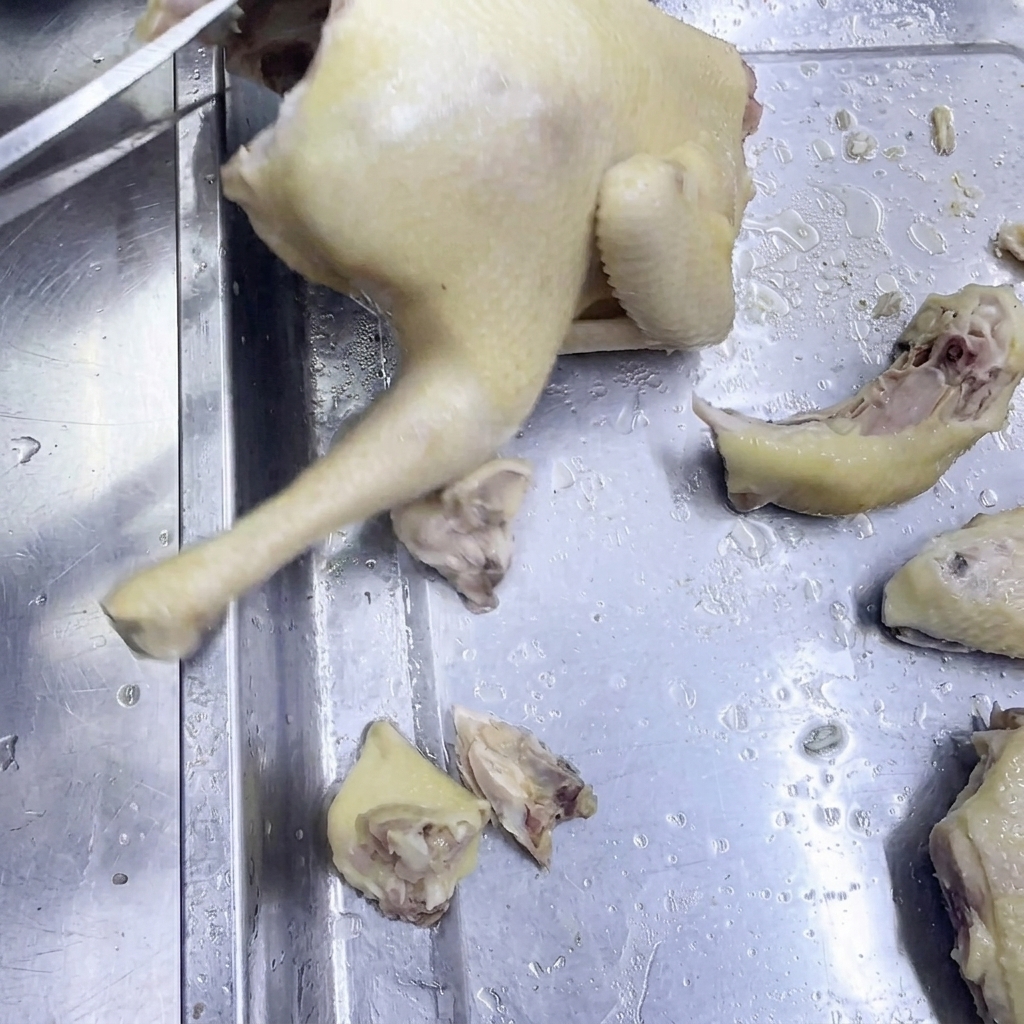 A pair of kitchen scissors cutting through cooked chicken on a stainless steel surface.