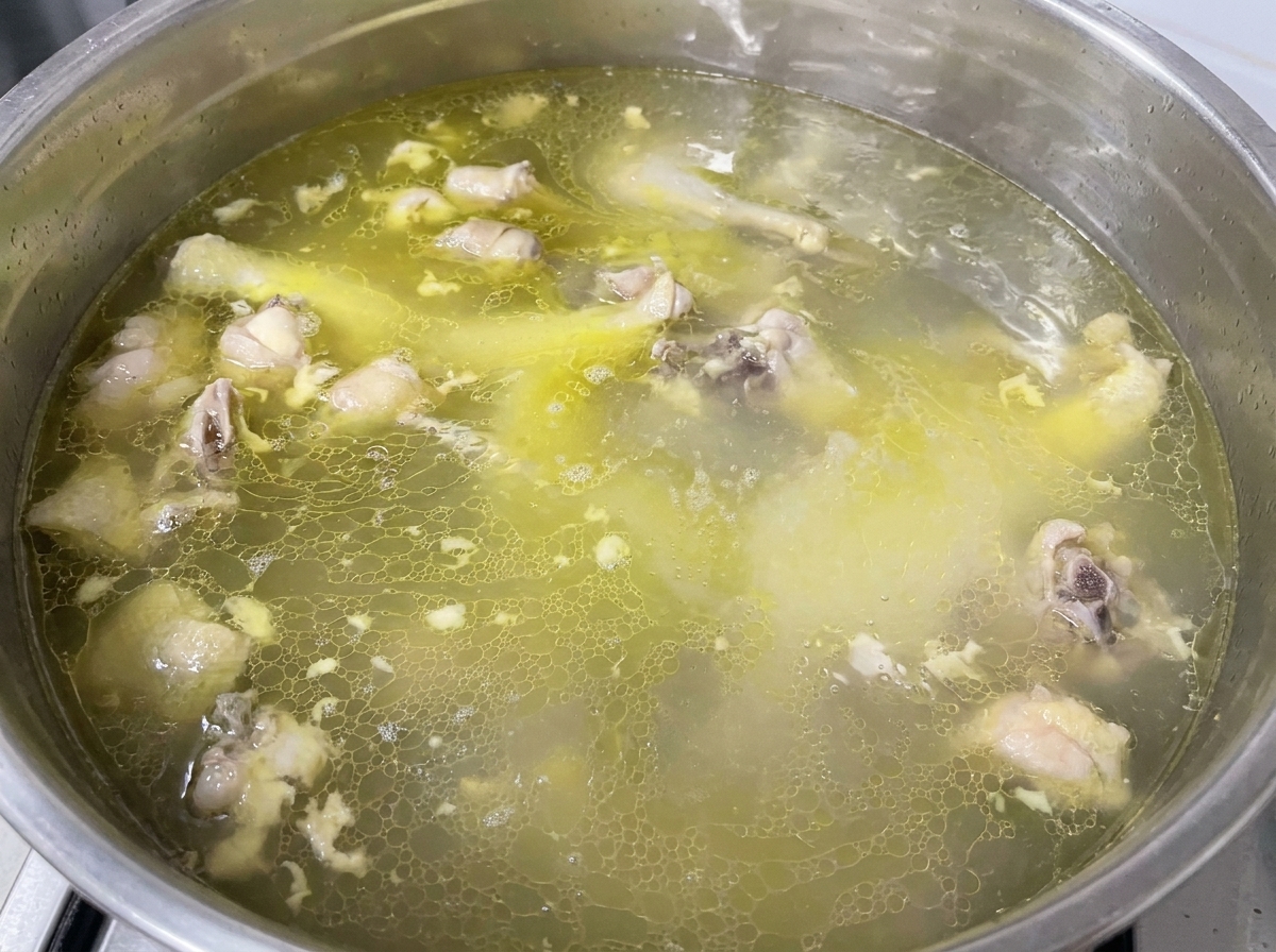 Seasoning being sprinkled into a pot of simmering golden chicken broth.