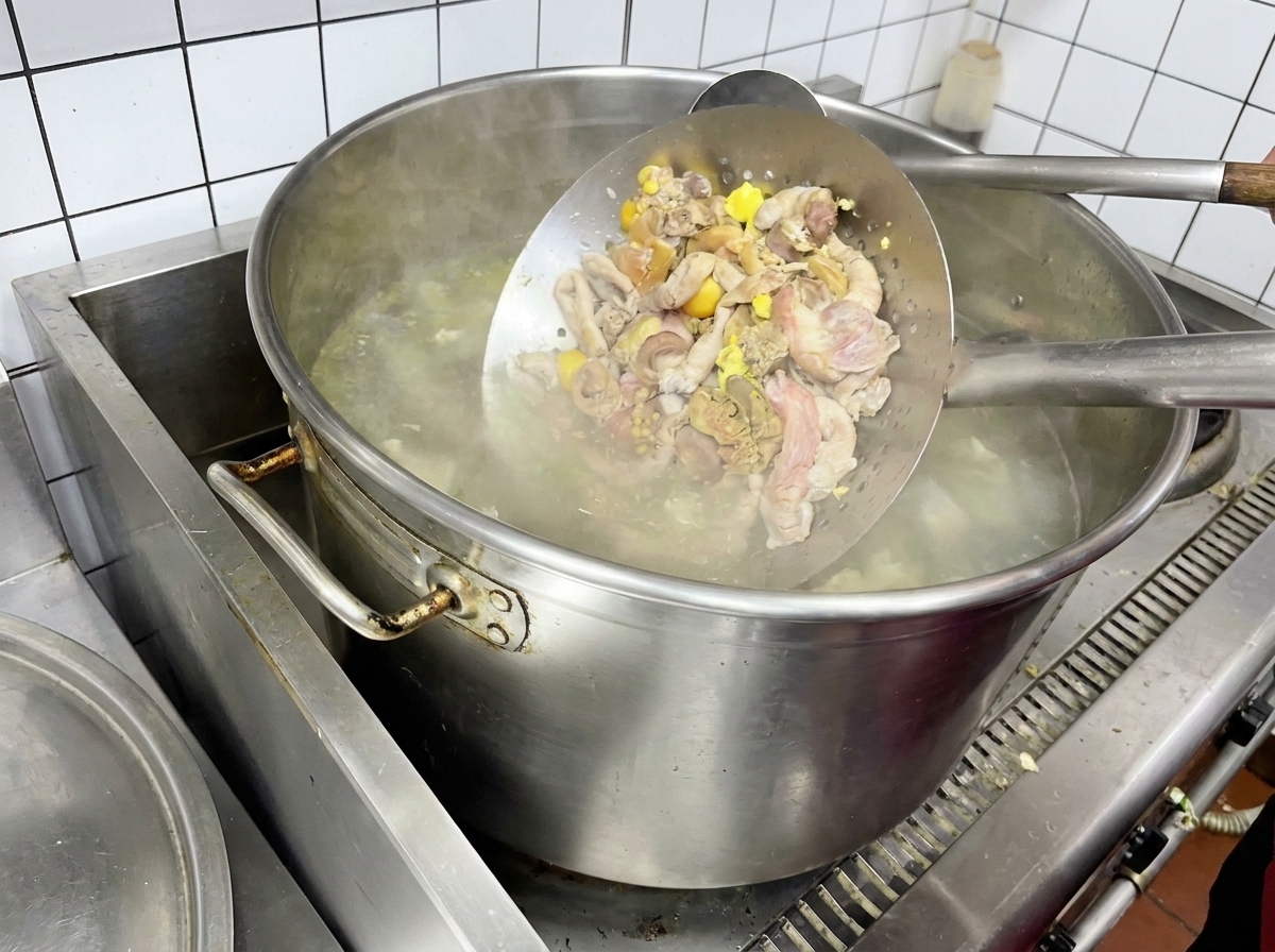 Chicken giblets being blanched in a metal strainer over boiling water.
