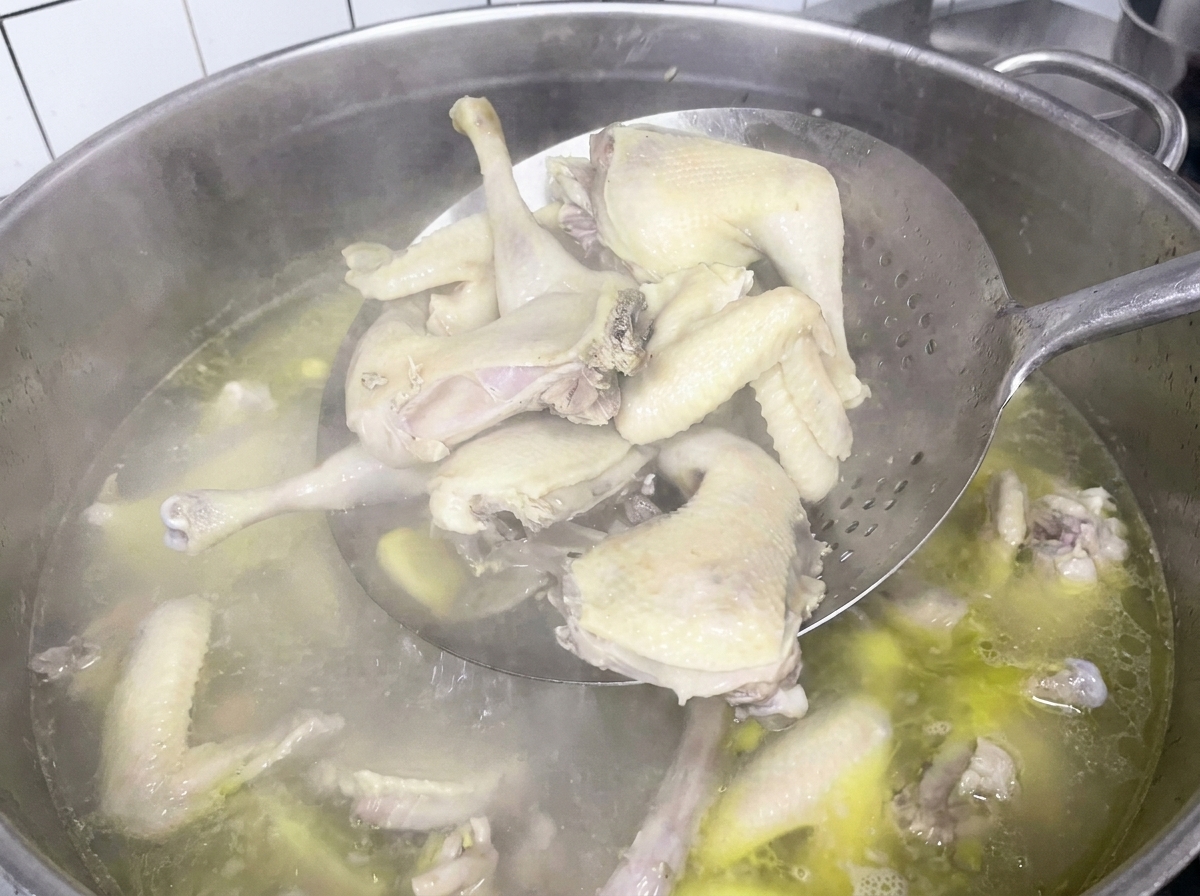 Boiled chicken pieces being scooped out of the pot with a spider strainer.