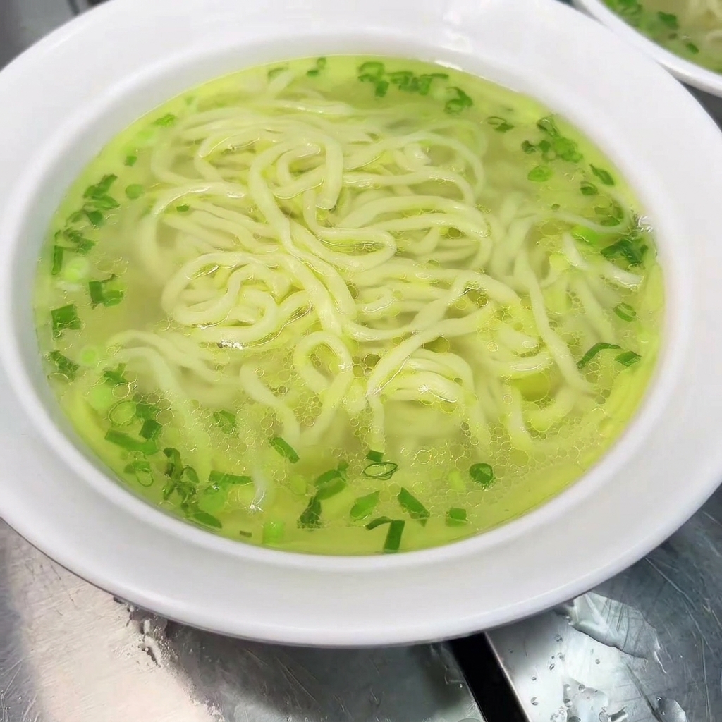 A bowl of noodles being garnished with a cooked chicken leg and hot broth.