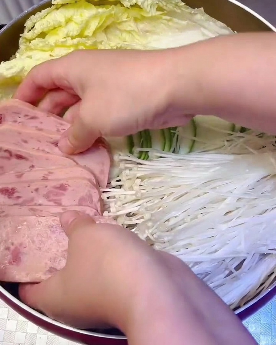 Sliced luncheon meat and enoki mushrooms being arranged systematically into the cooking pot.