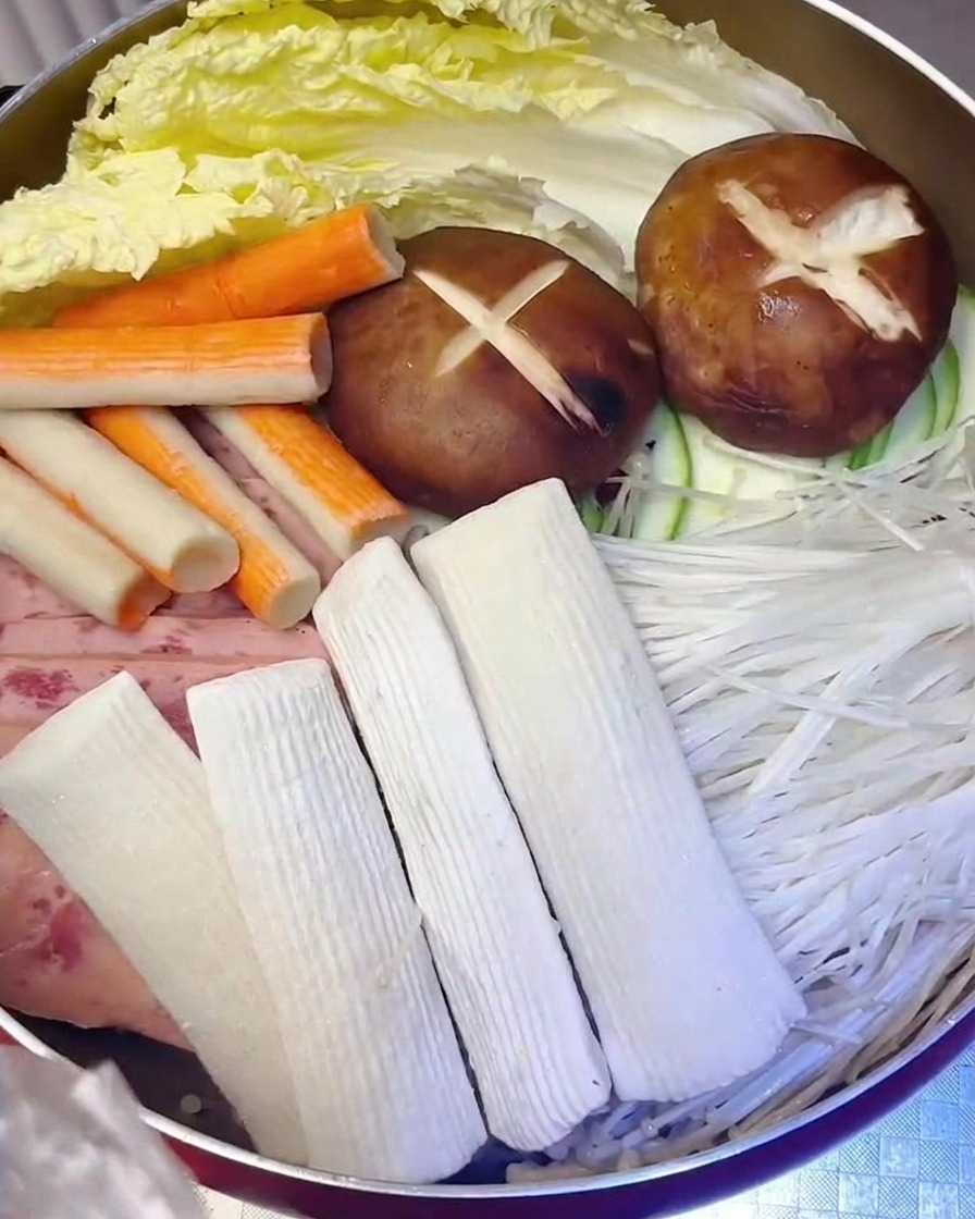 Fish cakes and crab sticks being carefully added to the pot alongside the meat and vegetables.