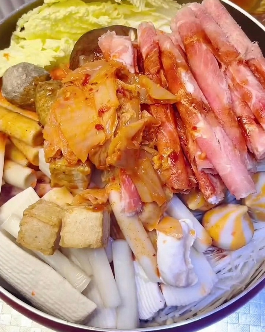A heap of chopped red kimchi being added to the pot with water being poured in.
