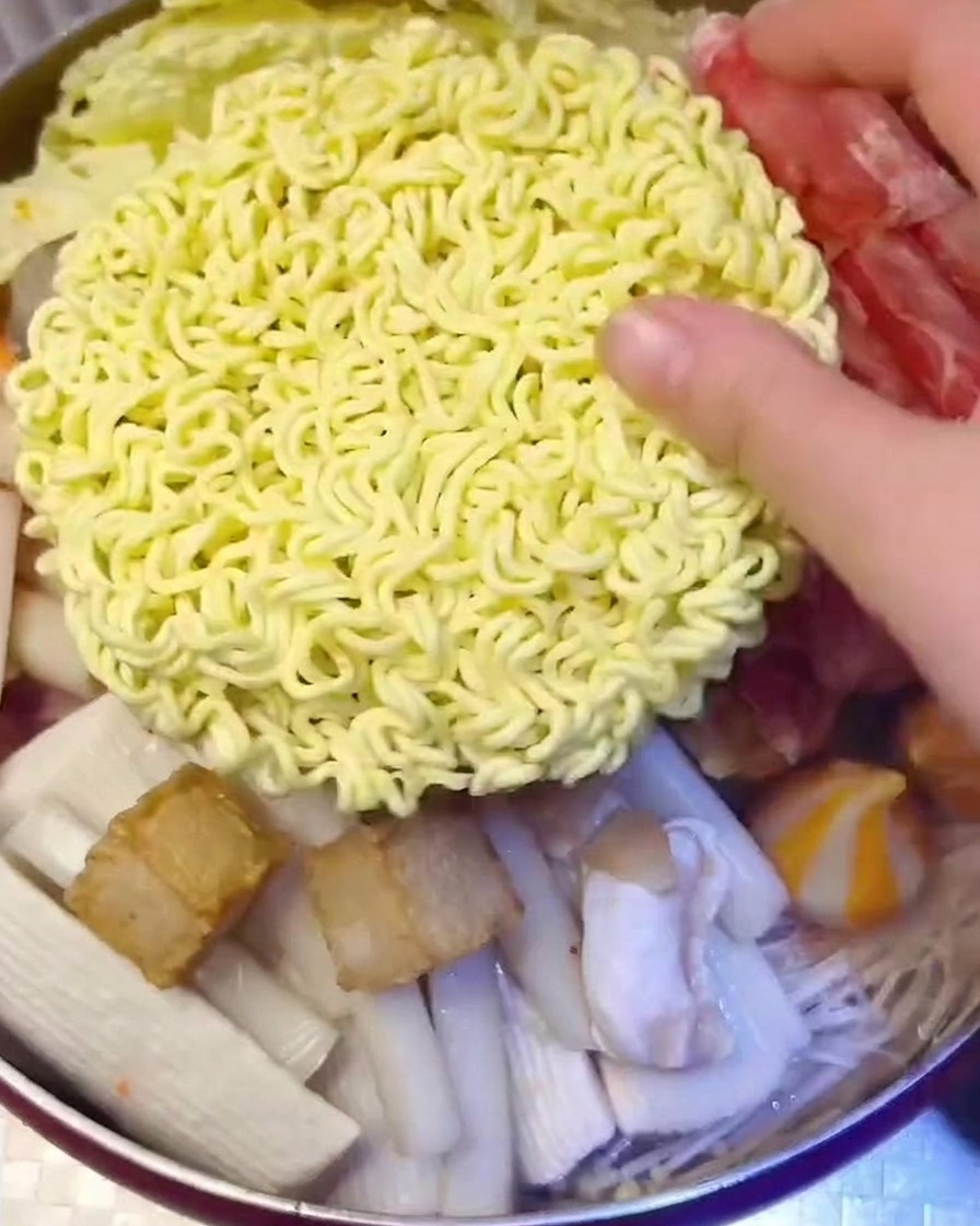 An instant noodle block topped with yellow cheese slices being placed into the pot.
