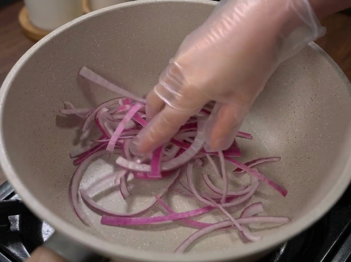 Onions and cabbage layered at the bottom of an empty cooking pot.