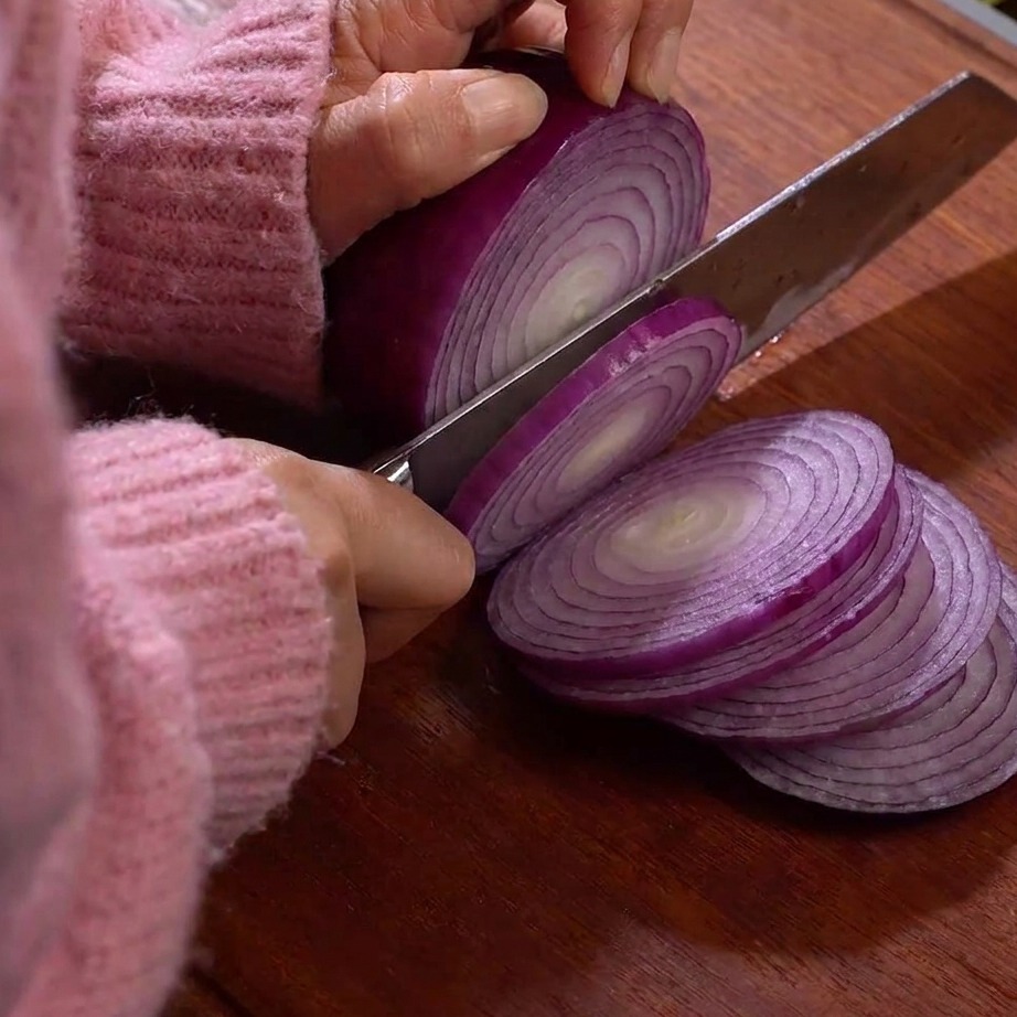 Thin slices of lotus root resting on a wooden cutting board.