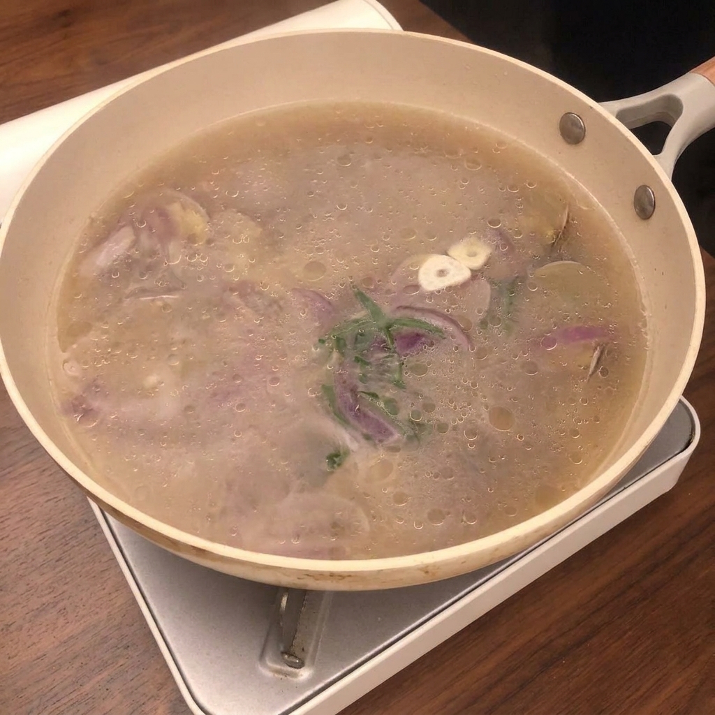 Clam cooking liquid being strained through a silver mesh sieve into a glass bowl.