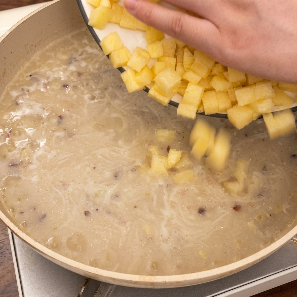 Hand dropping diced potato cubes into the pan of simmering soup.