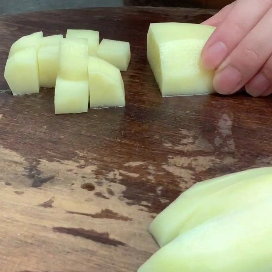 Peeled potato cut into small, even cubes on a wooden cutting board.