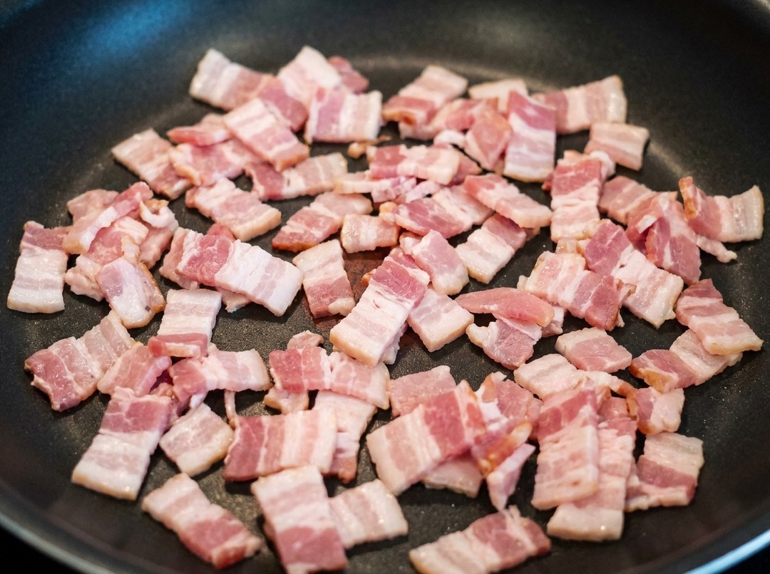 Bacon pieces frying in a pan, releasing flavorful fat.