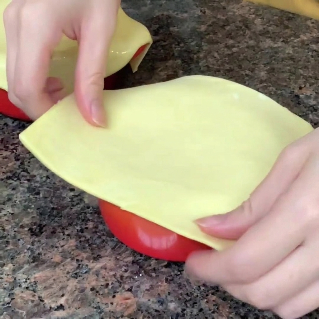 A sheet of puff pastry being placed and sealed over the rim of a bowl containing the chowder.
