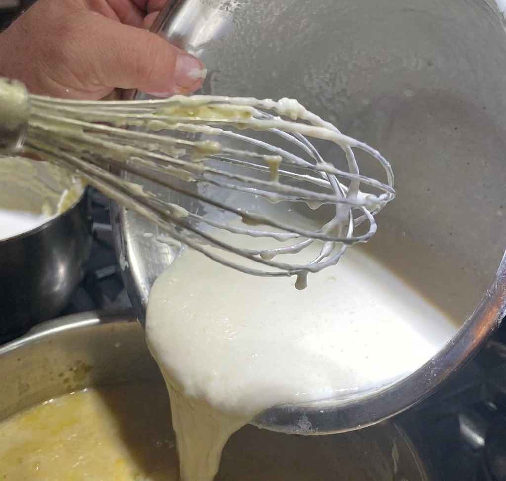 White pepper being sprinkled over a simmering pot of clam chowder base.