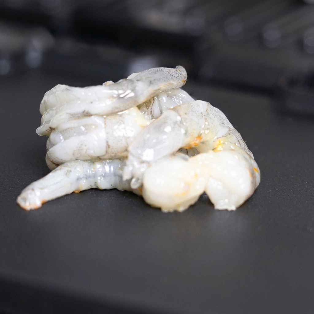 Fresh raw shrimp being arranged and turned on a clean section of the hot grill plate.