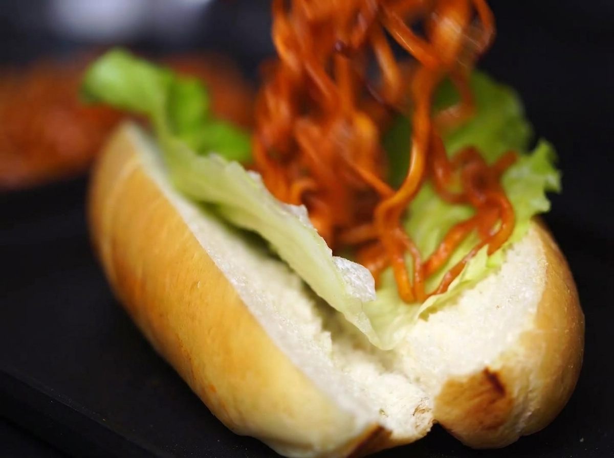 A large portion of saucy, cooked noodles being carefully added into the lettuce-lined bun.