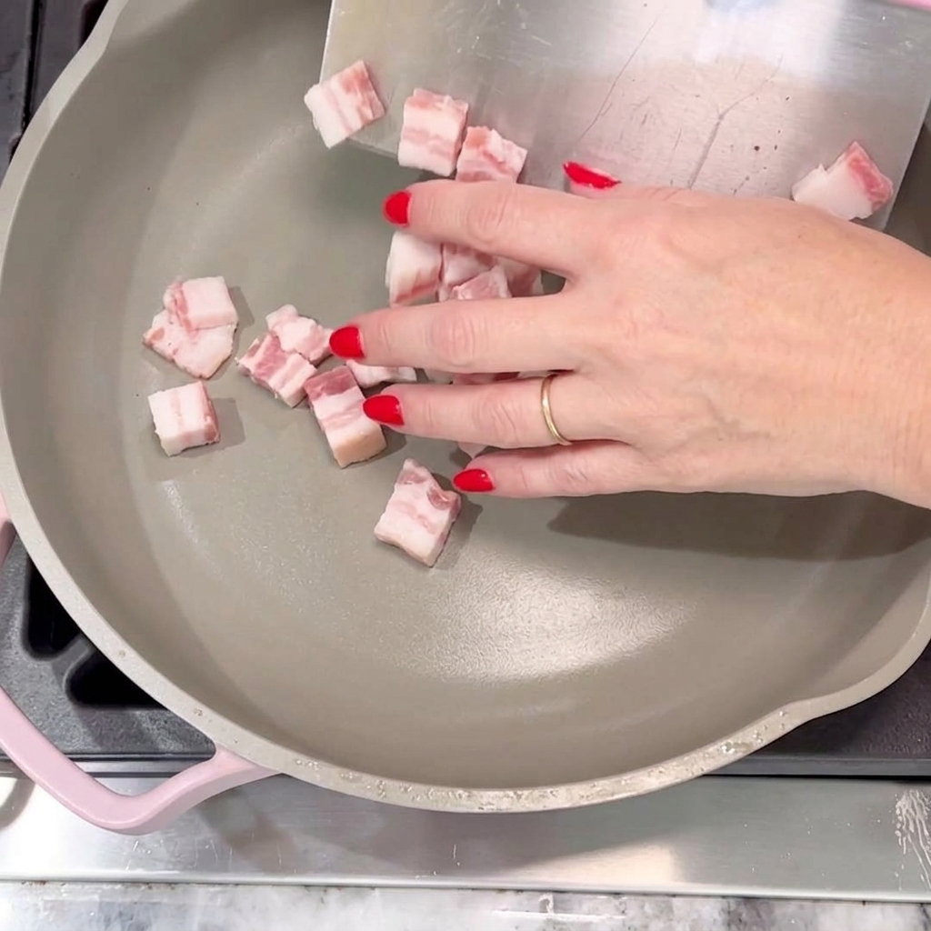 Bacon cubes being placed into a pan to fry until golden and crispy.