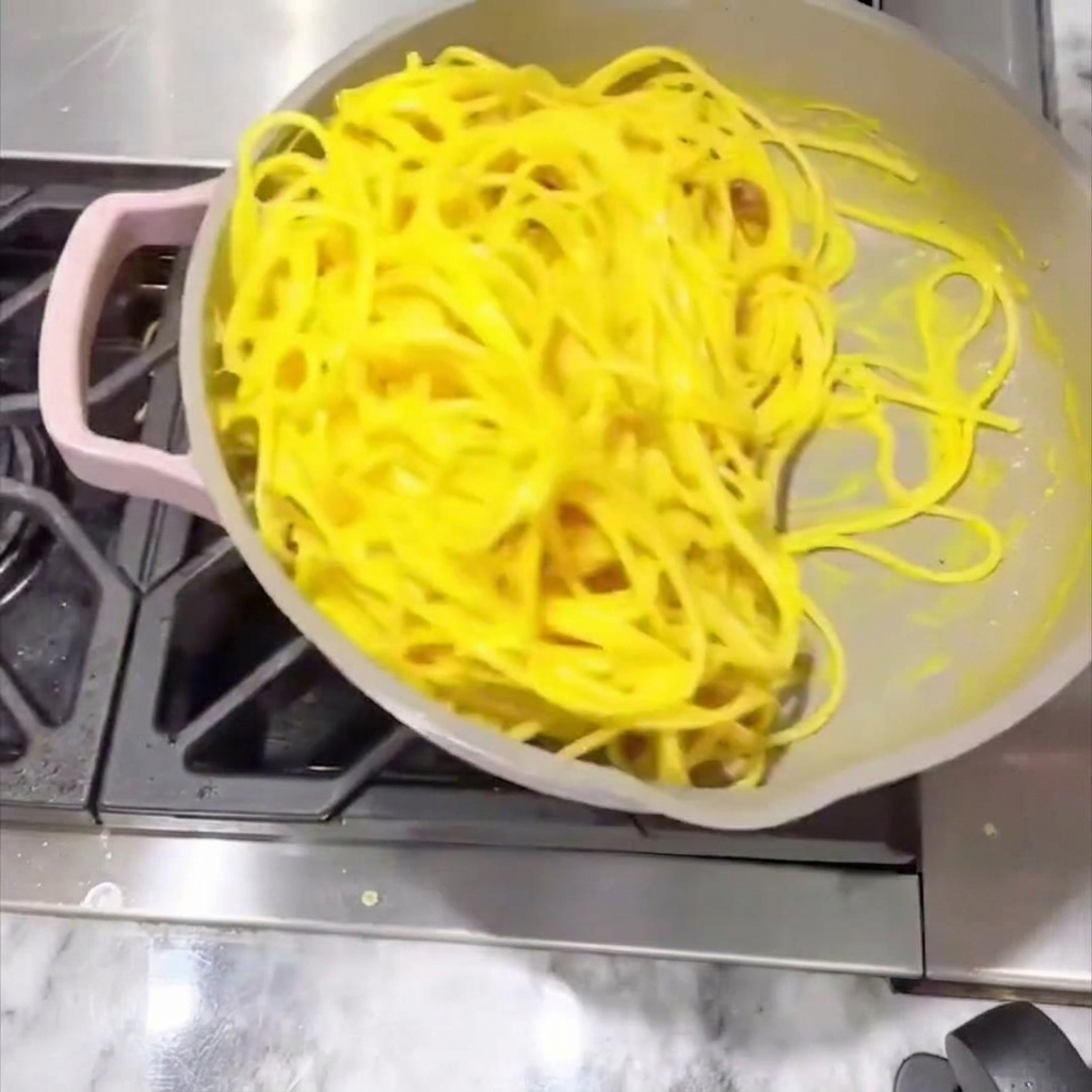 Spaghetti being stirred in the pan with a creamy sauce until evenly coated.