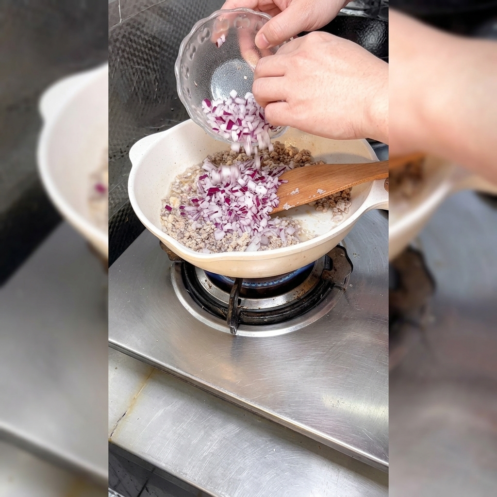 Diced onions being added to a pan filled with browned minced meat.